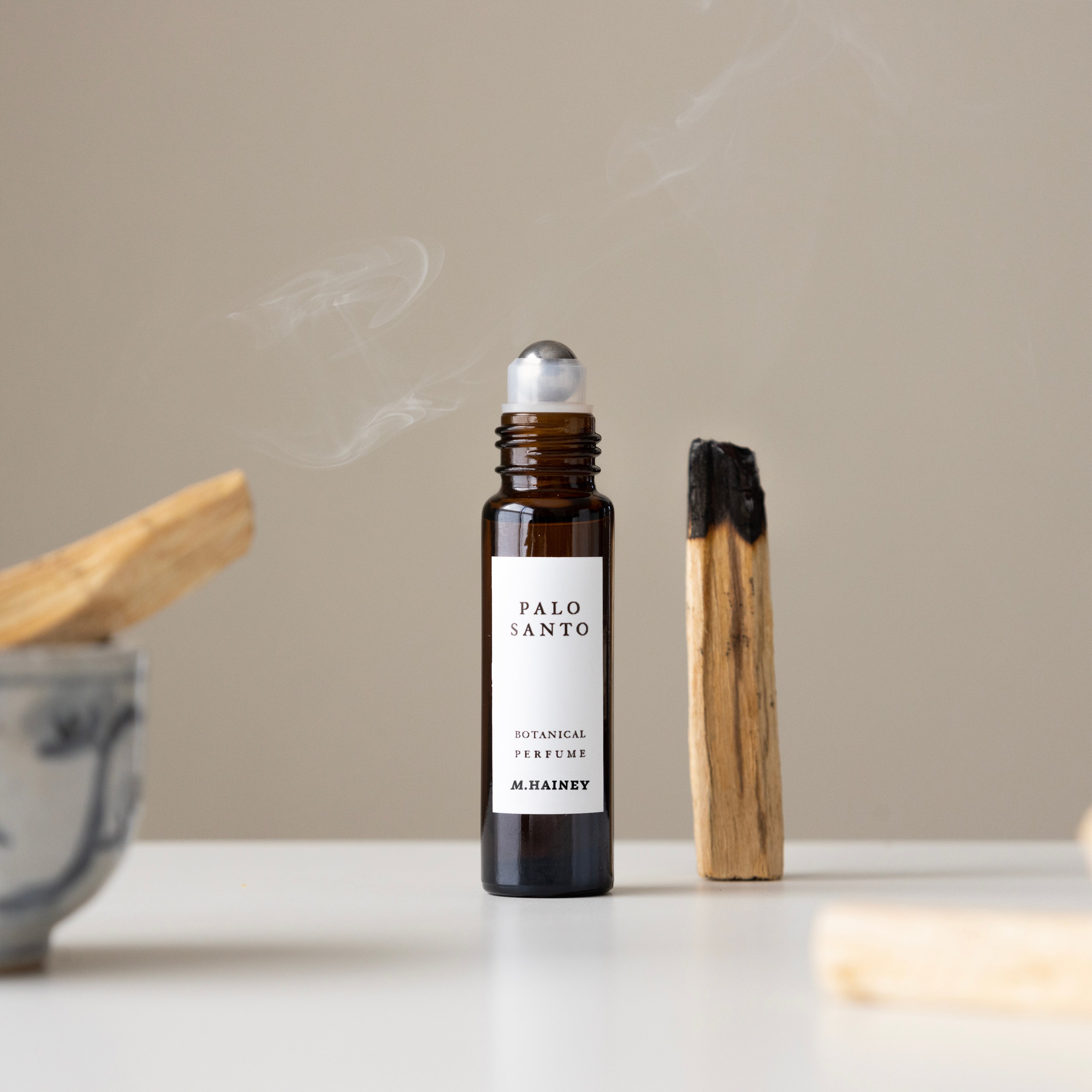 Palo Santo essential oil roller bottle with a lighter on a neutral background