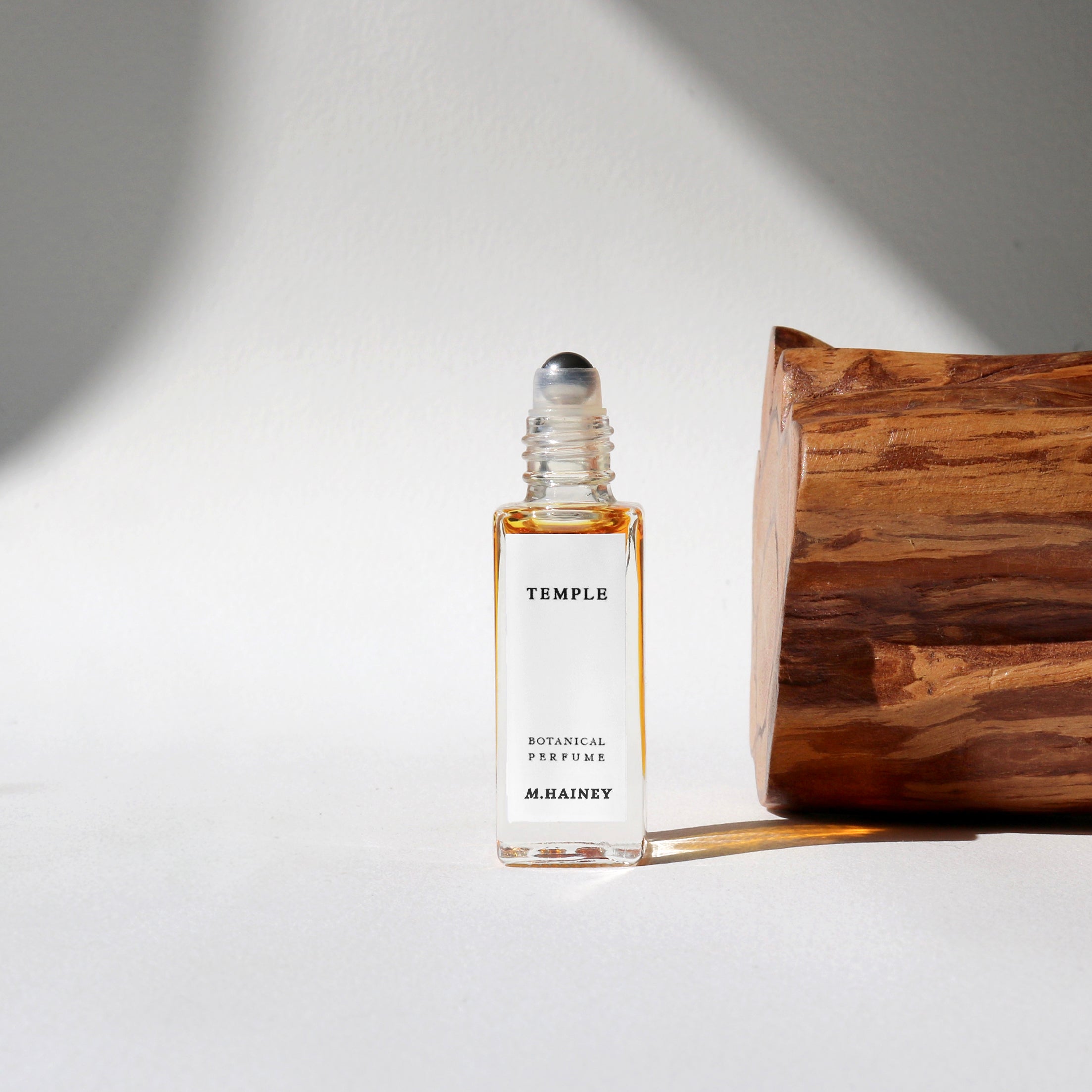 Roll-on perfume bottle labeled 'Temple M.HAINEY' on a light background with a wooden block.