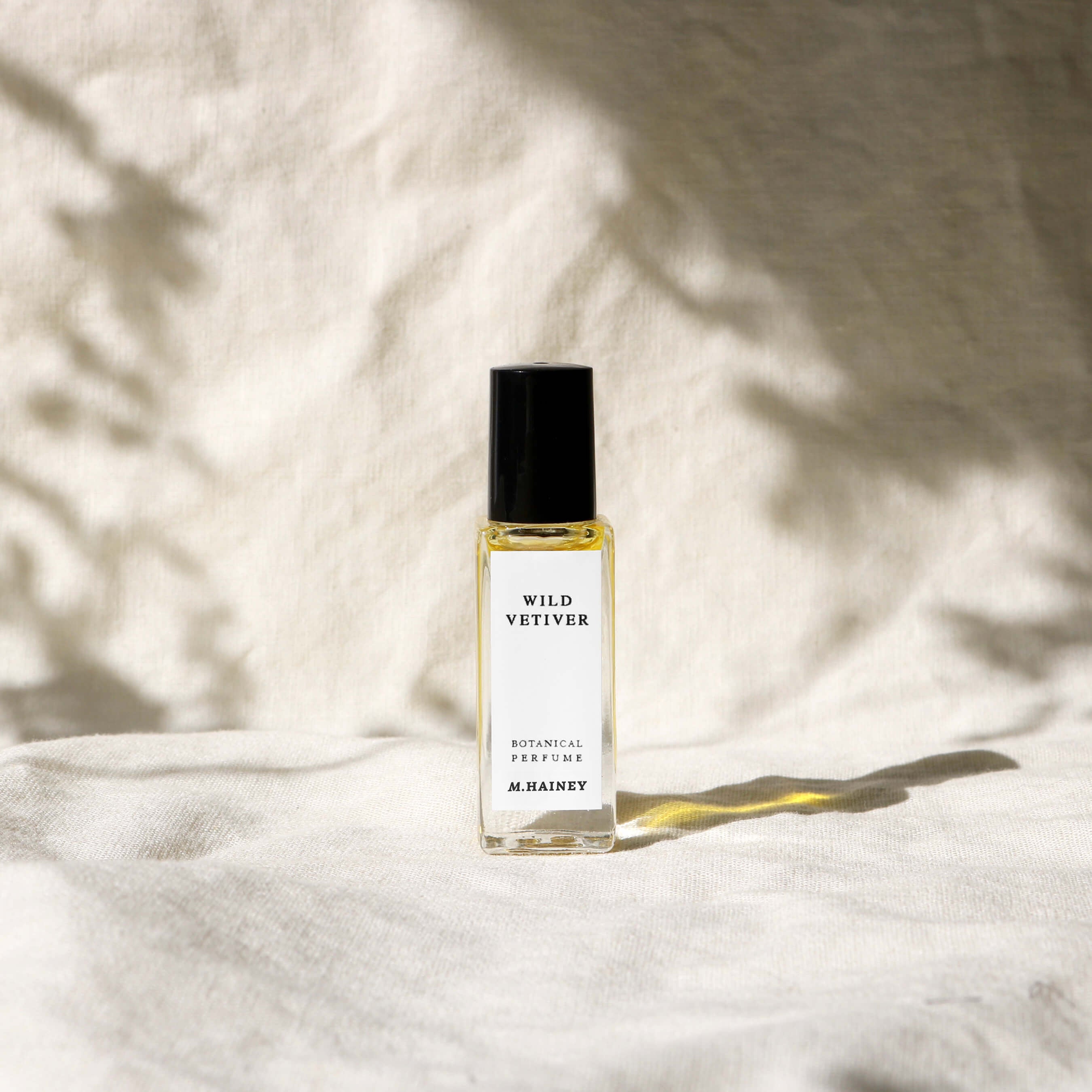 Perfume bottle labeled 'WILD VETIVER' by 'M.HAINEY' on a textured white surface with soft shadows.