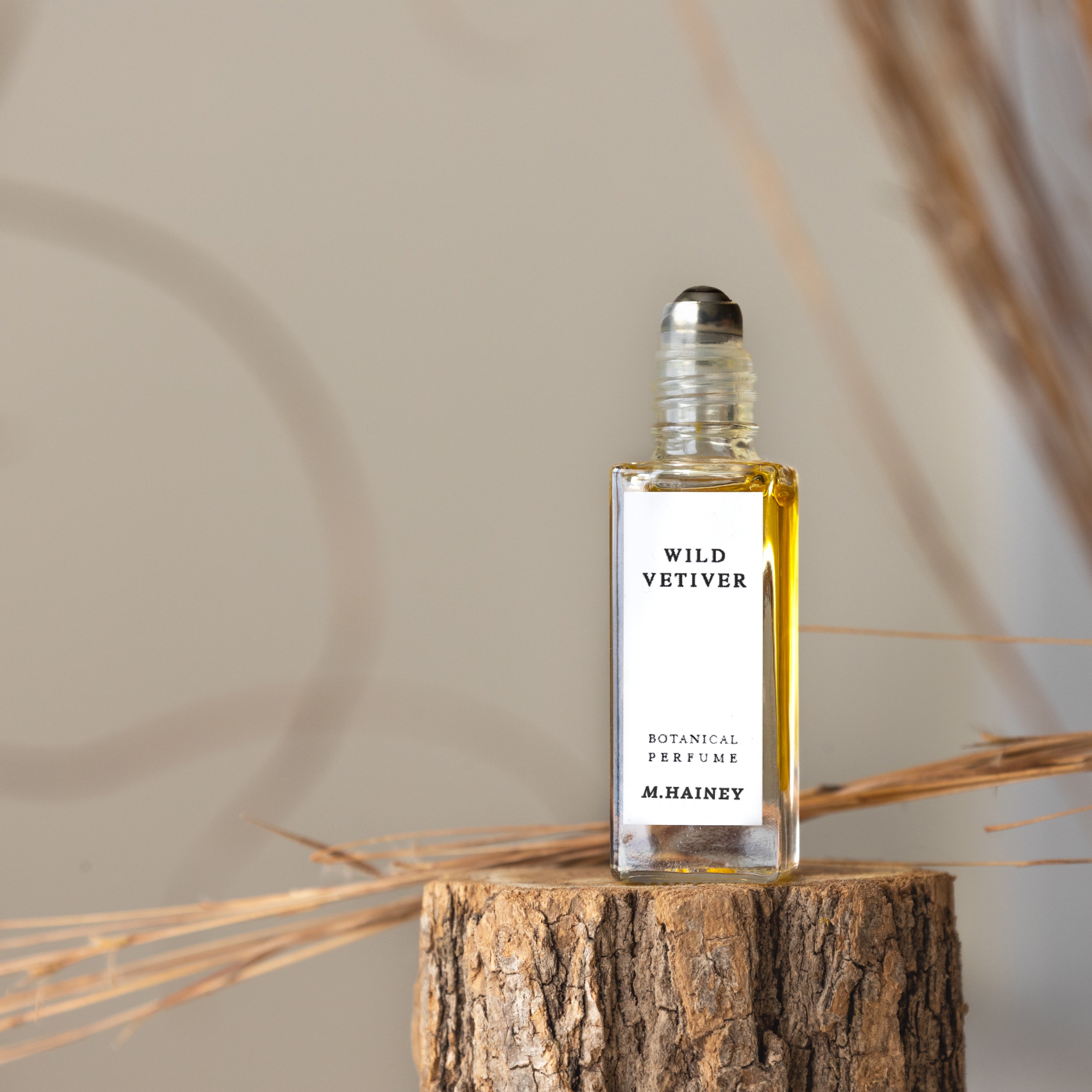 Roll-on perfume bottle labeled 'Wild Vetiver' by M. Hainey on a wooden block with dried plants in the background.