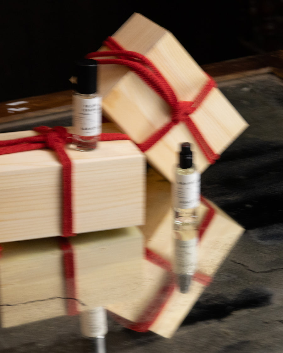Three wooden gift boxes tied with red ribbons and three small bottles on a reflective surface.