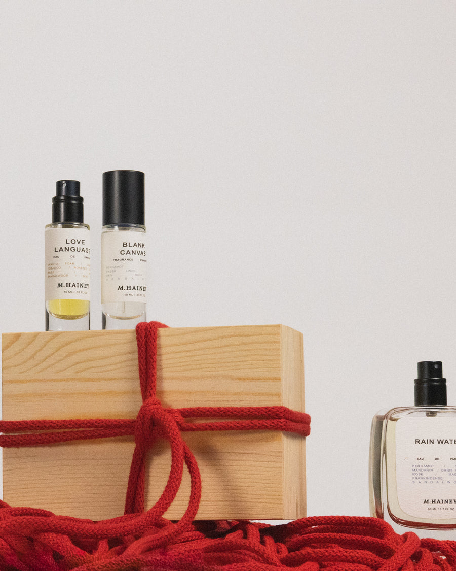 Three perfume bottles on a wooden block with red rope, against a white background
