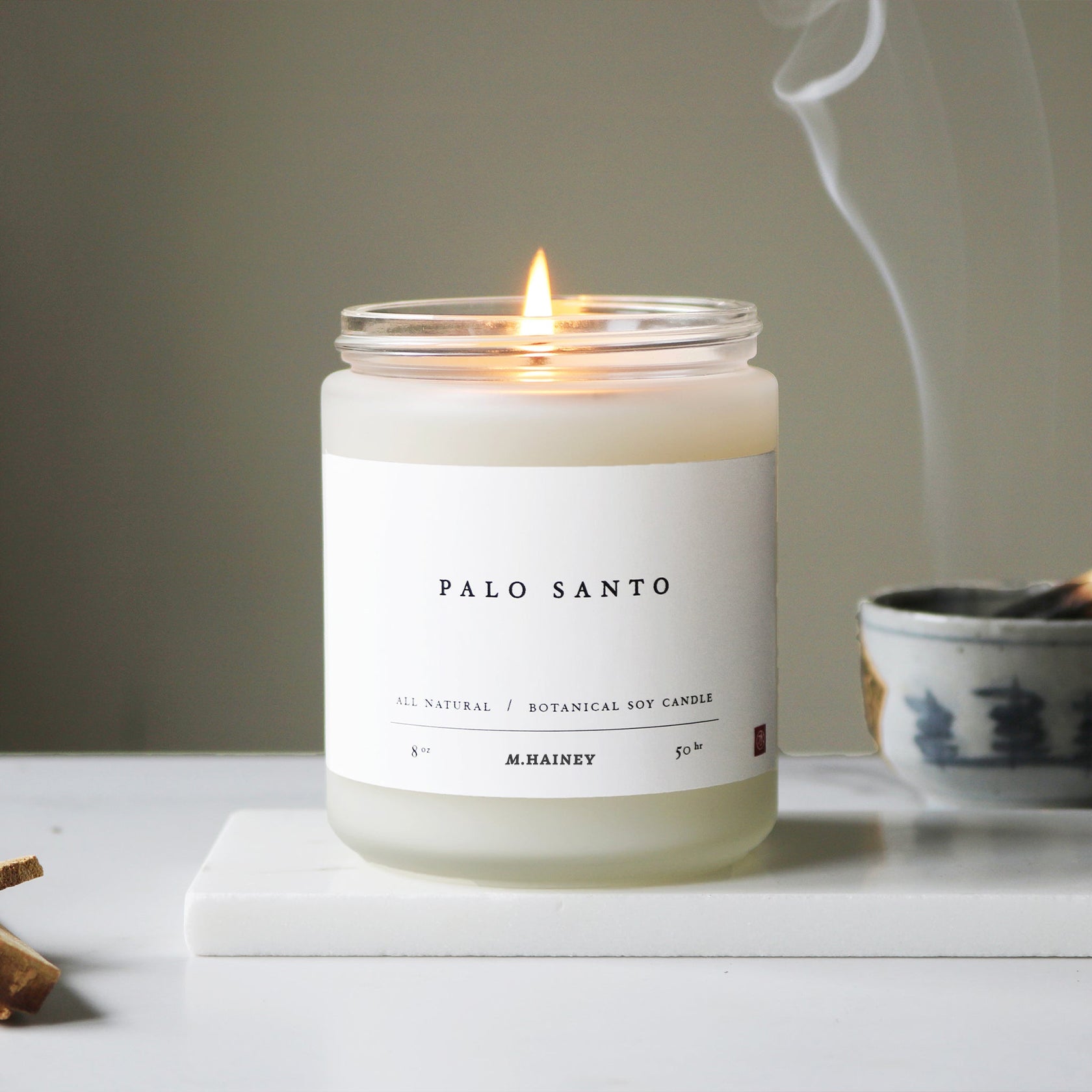 Palo Santo candle with a label on a white surface, with smoke in the background.